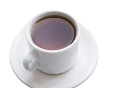 Tea With the Editor A top-down, high-angle view of a white ceramic teacup filled with dark amber tea or black coffee, resting on a matching round white saucer isolated on a plain background.