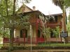 Walking through history at the Riley House The John G. Riley House, a historic two-story wood-frame home with wraparound porches, red railings, green shutters, and surrounding trees.