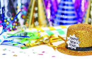 Rings in 2026 at Cascades Park Gold glitter top hat with a “Happy New Year!” label sits on a table surrounded by colorful party hats, streamers, and confetti, suggesting a New Year’s celebration.