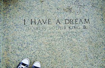 A timeline of notable events in the life of Martin Luther King, Jr. A photograph of engraved stone reading “I HAVE A DREAM – Martin Luther King Jr.”, referencing the March on Washington for Jobs and Freedom on August 28, 1963. The image is framed from above, with a pair of black-and-white sneakers visible at the bottom edge, creating a reflective, symbolic perspective on the historic inscription.