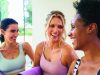 Tips to stay the course with a New Year’s resolution Three women in athletic wear smiling and talking indoors while holding rolled purple yoga mats, suggesting a friendly conversation before or after a fitness or yoga class in a bright, modern studio setting.