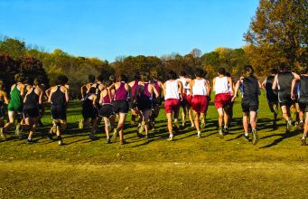 Tallahassee gearing up for major international sports weekend in January 2026 Group of high school cross-country runners seen from behind as they start a race across a grassy field with autumn trees in the background.