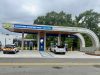 City opens first PowerTLH EV fast-charging station on Earth Day An outdoor electric vehicle charging station operated by the City of Tallahassee under a modern, curved canopy. A white Ford Mustang Mach-E and a white Chevrolet Bolt city utility vehicle are parked in charging bays. The canopy features digital signs displaying 'TALLAHASSEE SEE THE FUTURE TODAY' and 'PowerTLH' logos against a backdrop of trees and an overcast sky.