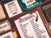 City of Tallahassee to host hurricane preparedness workshop in June A flat-lay view of emergency supplies arranged on a wooden table around a red clipboard with a 'Disaster Preparation List.' The checklist includes items like water, non-perishable food, a battery radio, batteries, a first aid kit, and matches. Surrounding the clipboard are physical prep items including boxes labeled 'Emergency Candles,' 'First Aid Kit,' and 'Matches,' alongside a clear container of batteries, a radio, a whistle, a pen, and a pair of pliers.
