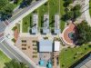 Remembering Smokey Hollow An aerial top-down view of Smokey Hollow Commemorative Park, featuring three open-frame house outline sculptures on green lawn, a brick circular plaza with a fountain, a central pavilion building, garden plots, and paved pedestrian walkways situated next to city streets.
