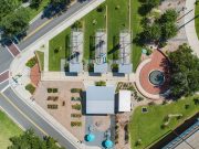 Remembering Smokey Hollow An aerial top-down view of Smokey Hollow Commemorative Park, featuring three open-frame house outline sculptures on green lawn, a brick circular plaza with a fountain, a central pavilion building, garden plots, and paved pedestrian walkways situated next to city streets.