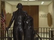 Leon County invites residents to rediscover local history during America 250 celebration A dark bronze full-body statue of George Washington in military uniform holding a walking cane, standing in a brightly lit government building corridor. In the background, an American flag and a state flag stand next to a hallway wall bearing the text 'Governor' and 'Lt. Governor'.