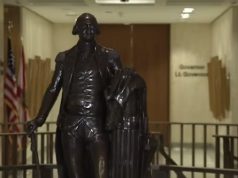 Leon County invites residents to rediscover local history during America 250 celebration A dark bronze full-body statue of George Washington in military uniform holding a walking cane, standing in a brightly lit government building corridor. In the background, an American flag and a state flag stand next to a hallway wall bearing the text 'Governor' and 'Lt. Governor'.