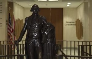Leon County invites residents to rediscover local history during America 250 celebration A dark bronze full-body statue of George Washington in military uniform holding a walking cane, standing in a brightly lit government building corridor. In the background, an American flag and a state flag stand next to a hallway wall bearing the text 'Governor' and 'Lt. Governor'.